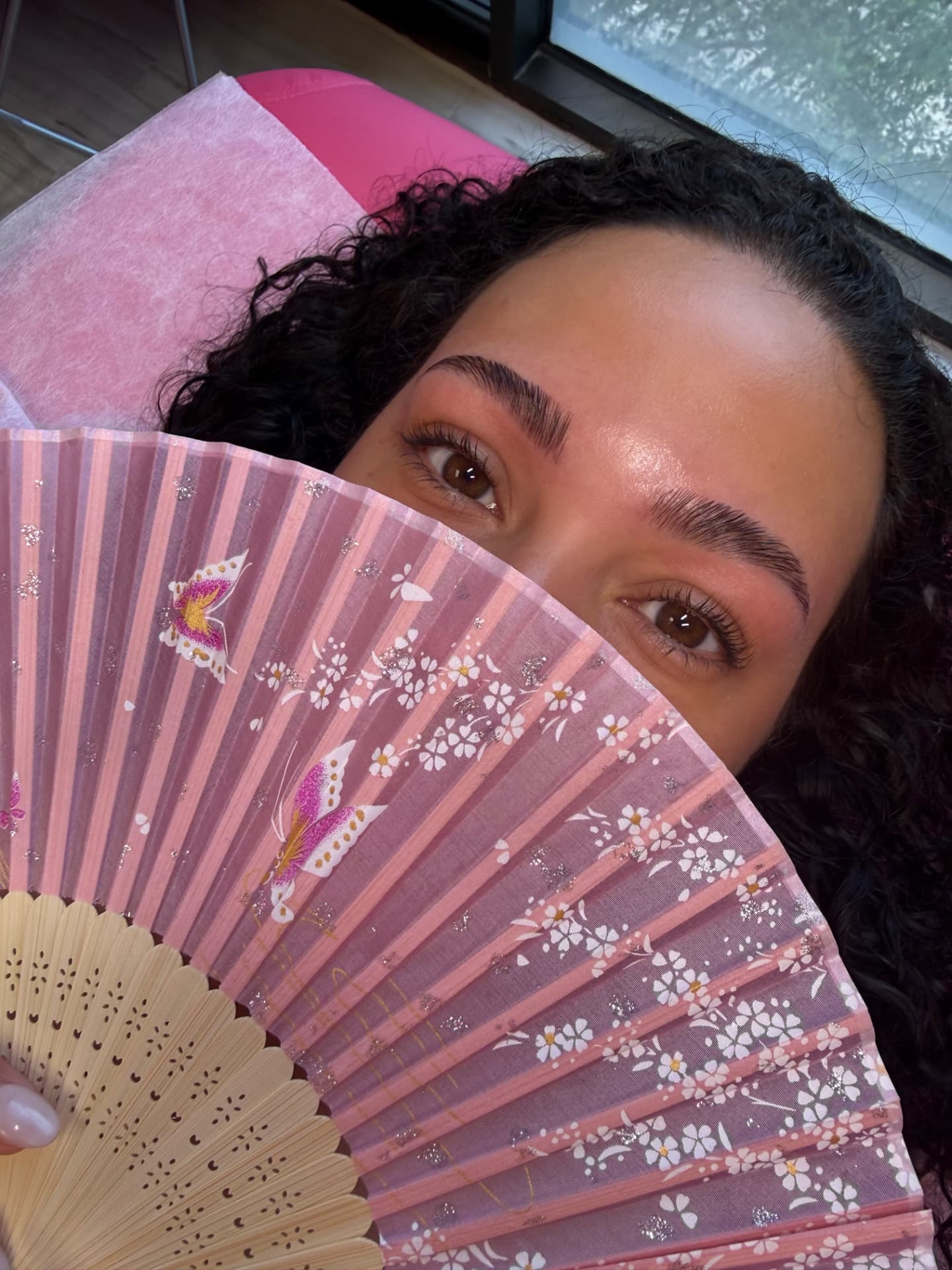 Client with freshly laminated brows holding a pink fan